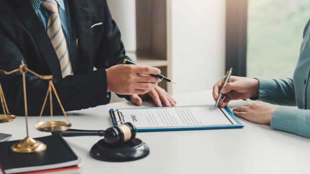 Close-up of a businessman hand pointing at a document to a client holding a pen to sign contract documents at the office.